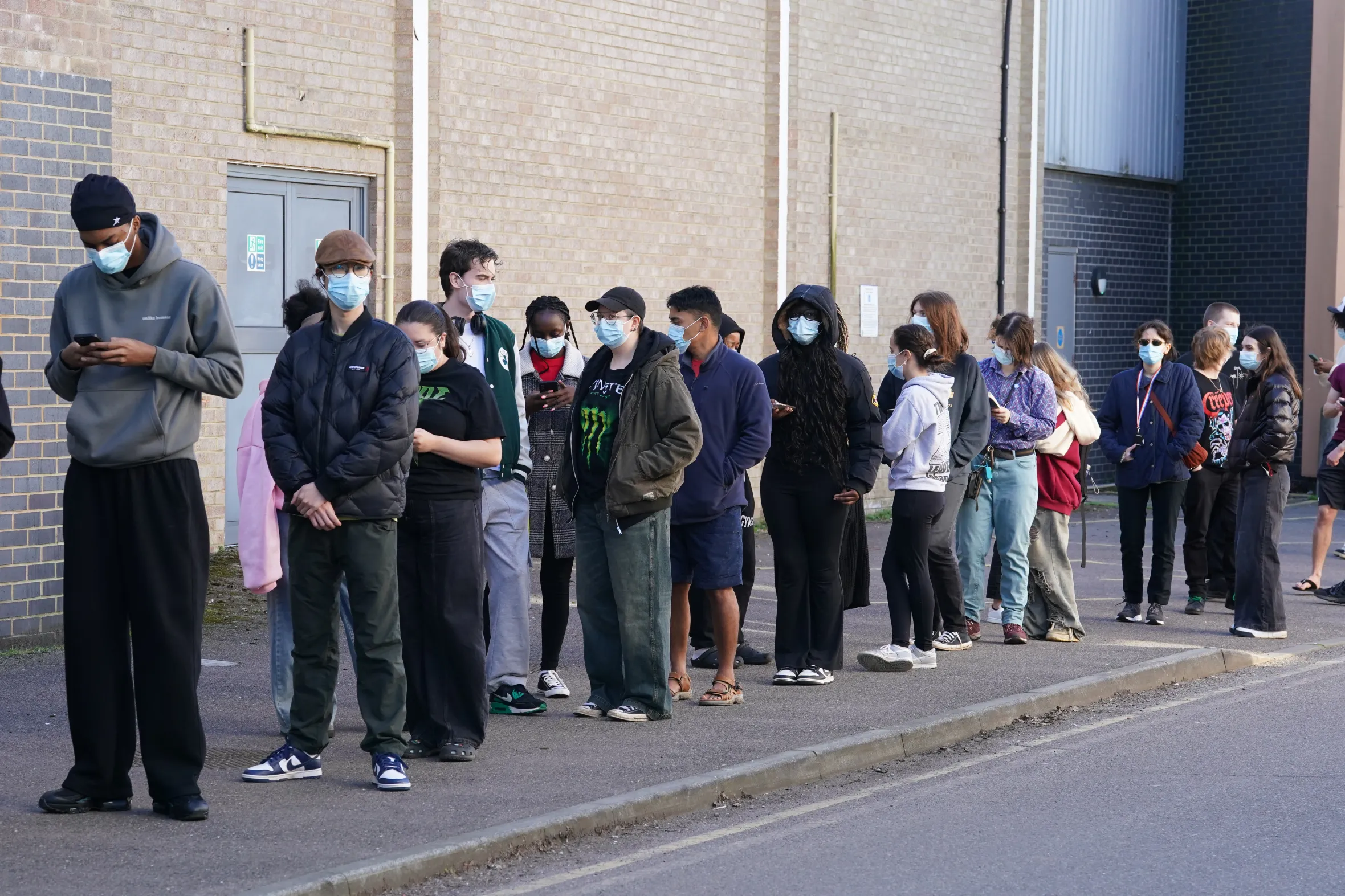 Students wearing face masks queue outside a building at the University of Kent for meningitis B vaccinations.