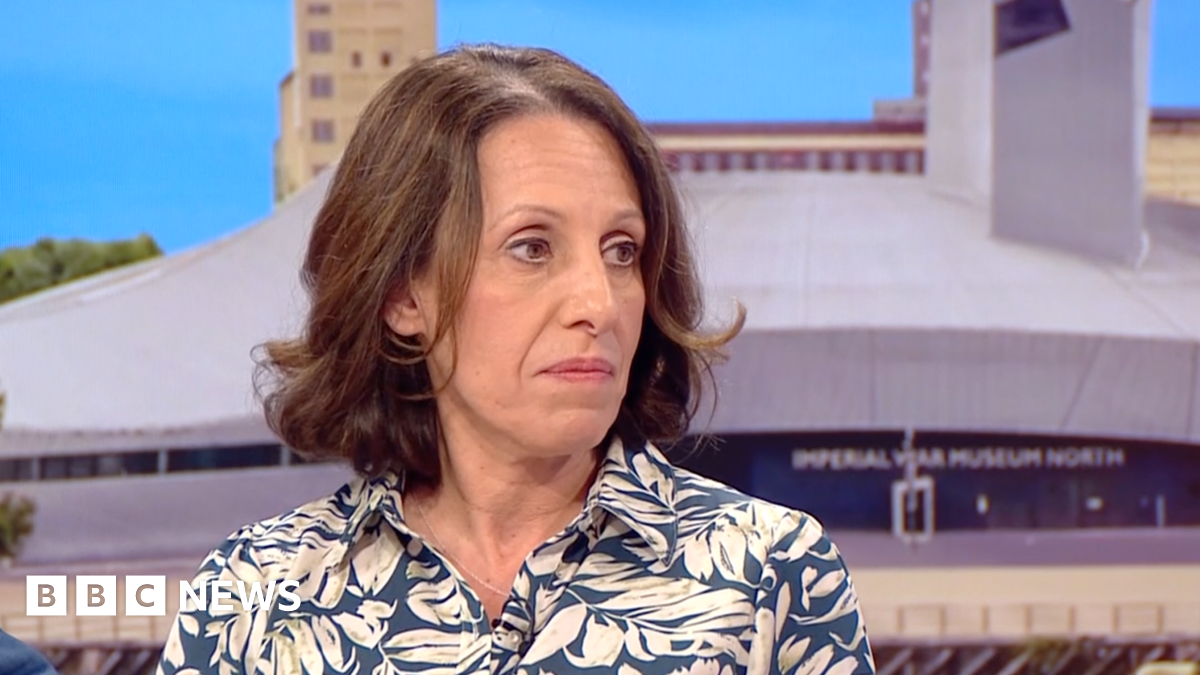 Shirine Khoury-Haq with short brown hair, earing a blue shirt with a white leaf print on it, sitting on the BBC Breakfast sofa with the Imperial War Museum North seen behind her