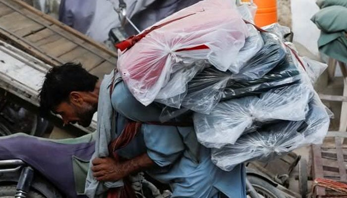 A labourer bends over as he carries packs of textile fabric on his back to deliver to a nearby shop in a market in Karachi. — Reuters/FIle