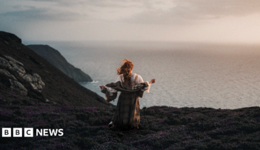 Ciara stands wearing traditional Celtic clothing on the edge of a cliff looking out to sea.