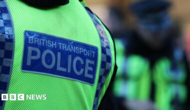 The back of a British Transport Police officer who is wearing a high viz yellow stab vest.