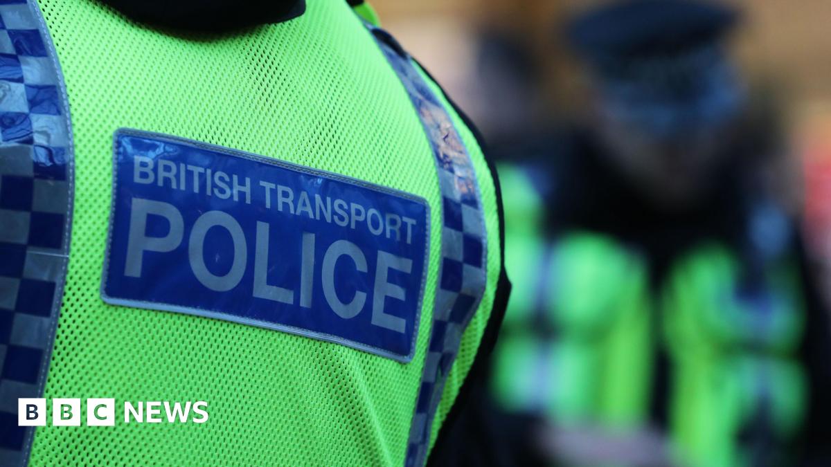 The back of a British Transport Police officer who is wearing a high viz yellow stab vest.