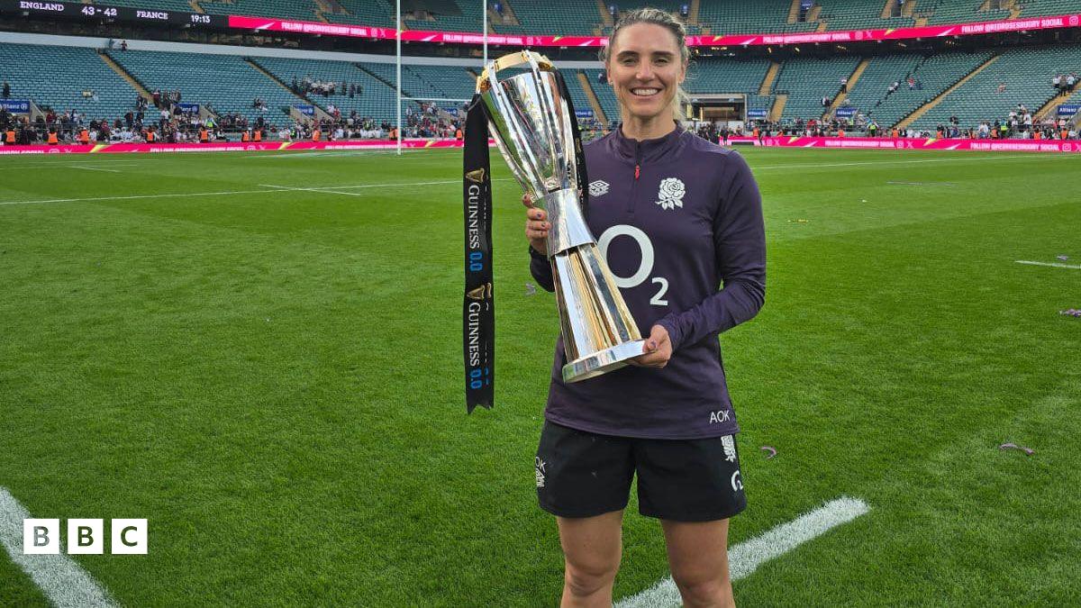Aimee Ellen O'Keeffe standing at Twickenham holding a rugby trophy which the Red Roses had won