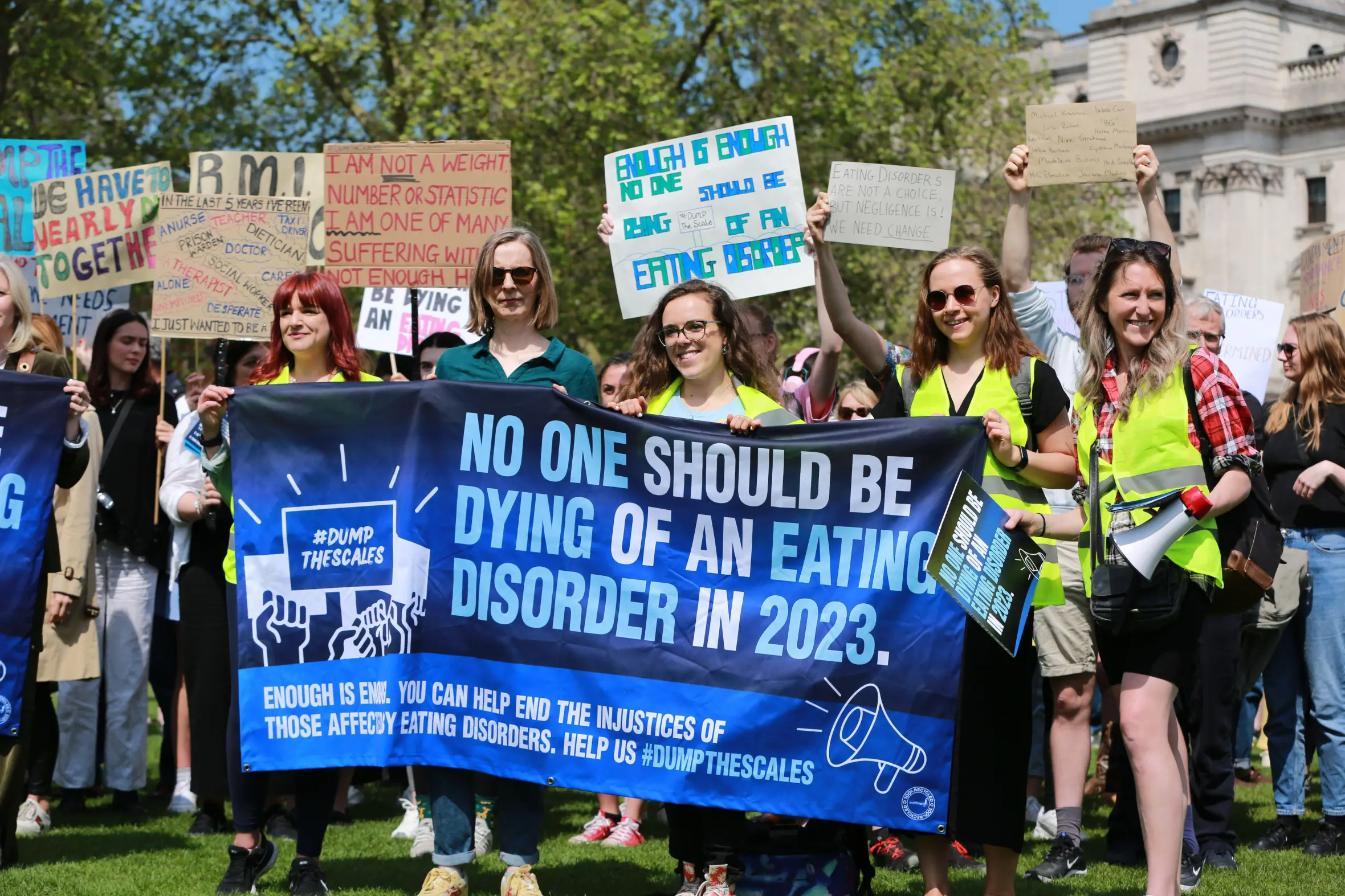 Protesters at a "March for People Affected by Eating Disorders" holding signs and a large banner that reads, "NO ONE SHOULD BE DYING OF AN EATING DISORDER IN 2023."