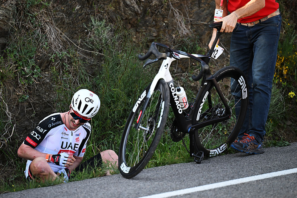 Jay Vine sat in a culvert while a helper picks up his bike after a crash