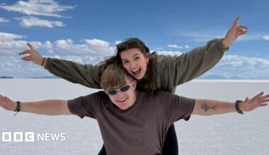 Cathie and Tricia pictured holding a glass of champagne each. They are both smiling. Tricia has her arm around Cathie.