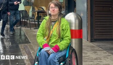 A wheelchair user in a green coat and blue jeans, sat outside a Subway station