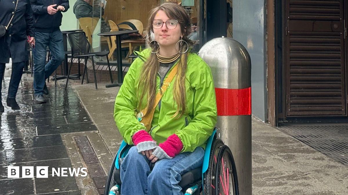 A wheelchair user in a green coat and blue jeans, sat outside a Subway station