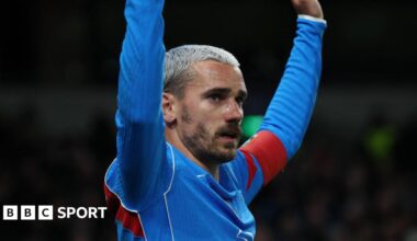 Atletico Madrid forward Antoine Griezmann, with bleached blond hair and facial hair, has both arms raised as he wears blue and red kit