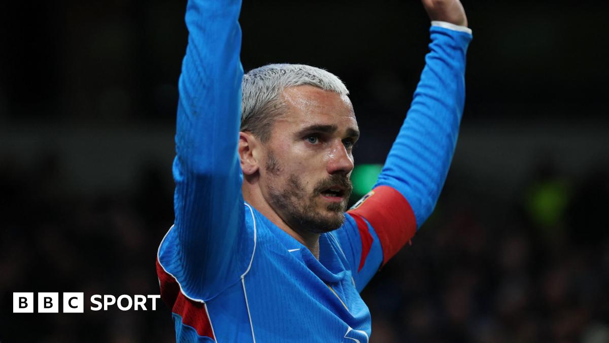 Atletico Madrid forward Antoine Griezmann, with bleached blond hair and facial hair, has both arms raised as he wears blue and red kit