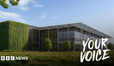 A large data centre building. It is mostly glass windows with trees dotted around in front of the building