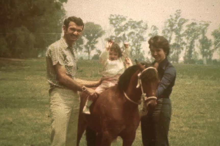 A young Gabriela sitting on a horse with her parents on either side smiling