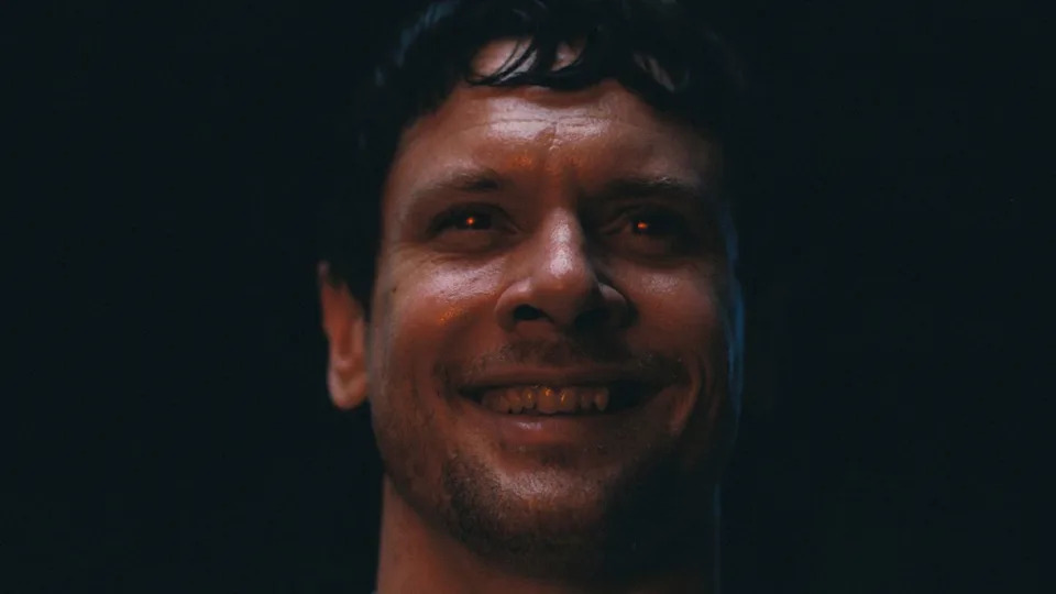  Jack O'Connell smiles gleefully with glowing red eyes in Sinners. . 