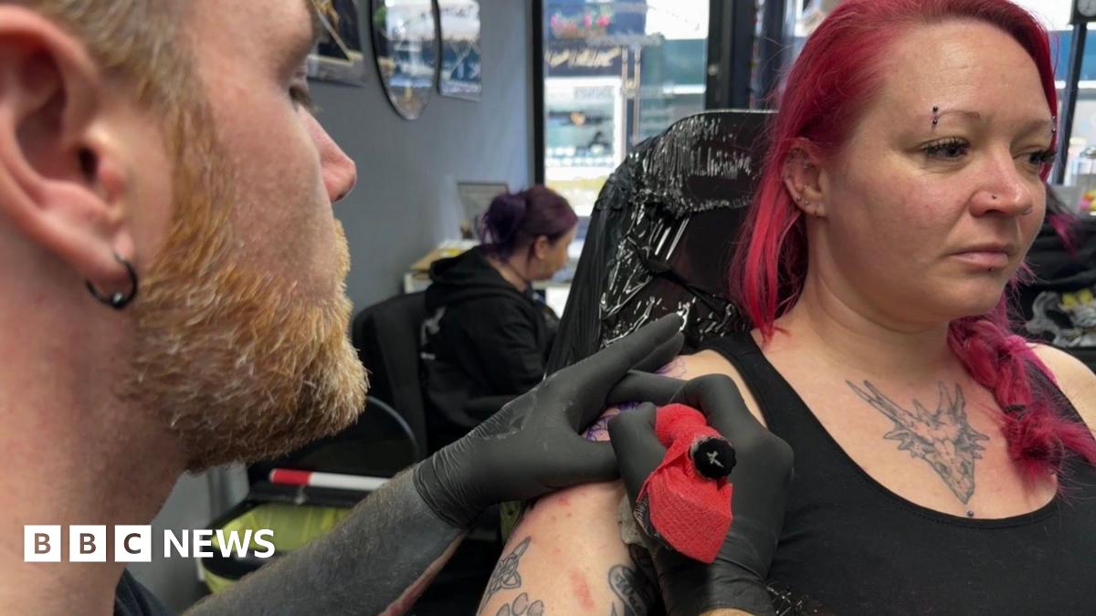 A woman with pink hair having a tattoo done.