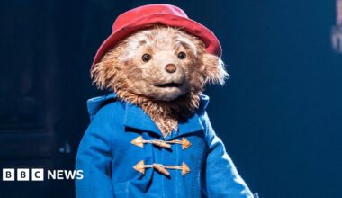 Paddington Bear on stage in Paddington The Musical, wearing a blue jacket