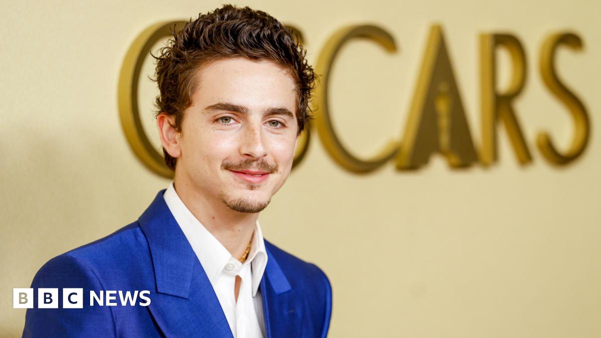 Timothee Chalamet in a bright blue suit and white shirt, posing in front of the word Oscars on a wall in large gold letters, at the 98th Oscars Nominees Luncheon at the Beverly Hilton Hotel on 10 February 2026