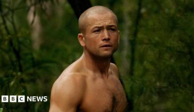 Egerton topless in a forest. He also ahs a shaved head
