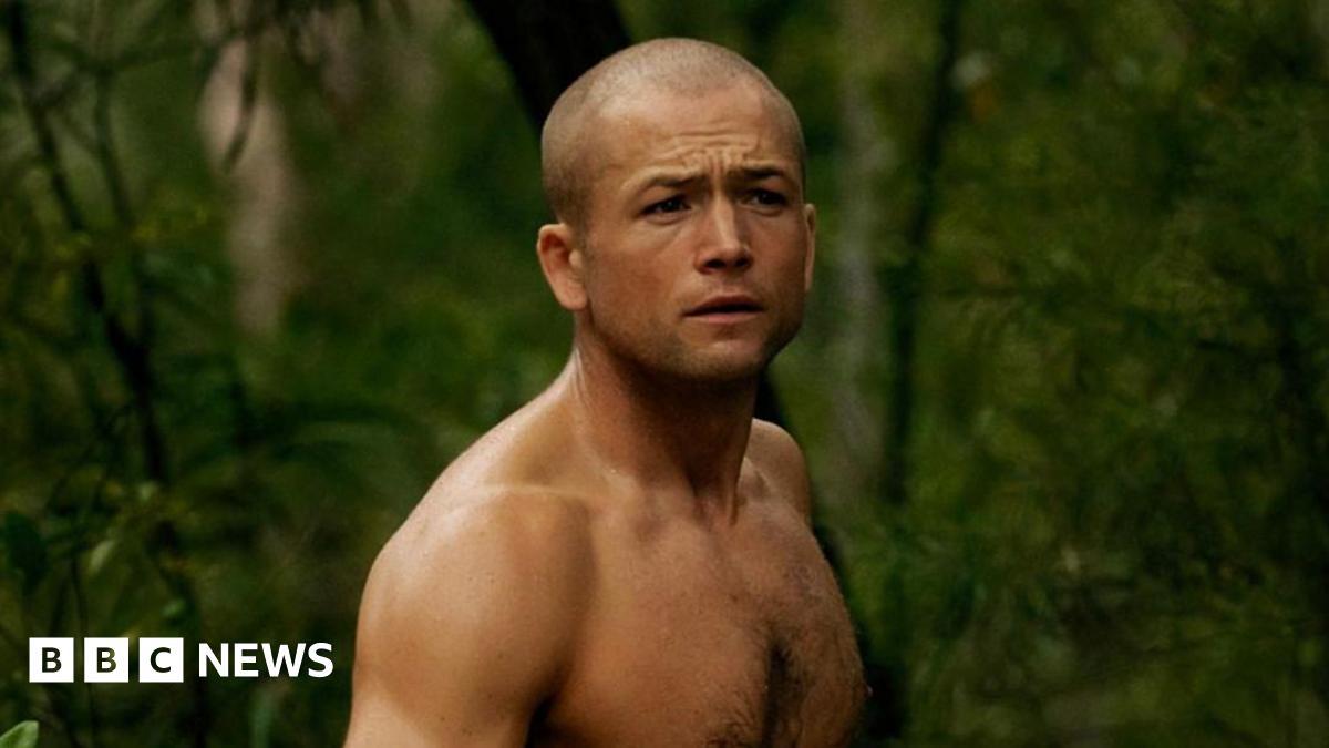 Egerton topless in a forest. He also ahs a shaved head