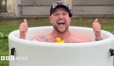 Image of Harry Beattie in a round ice bath, smiling at the camera with his thumbs up, all he is wearing is a black cap.