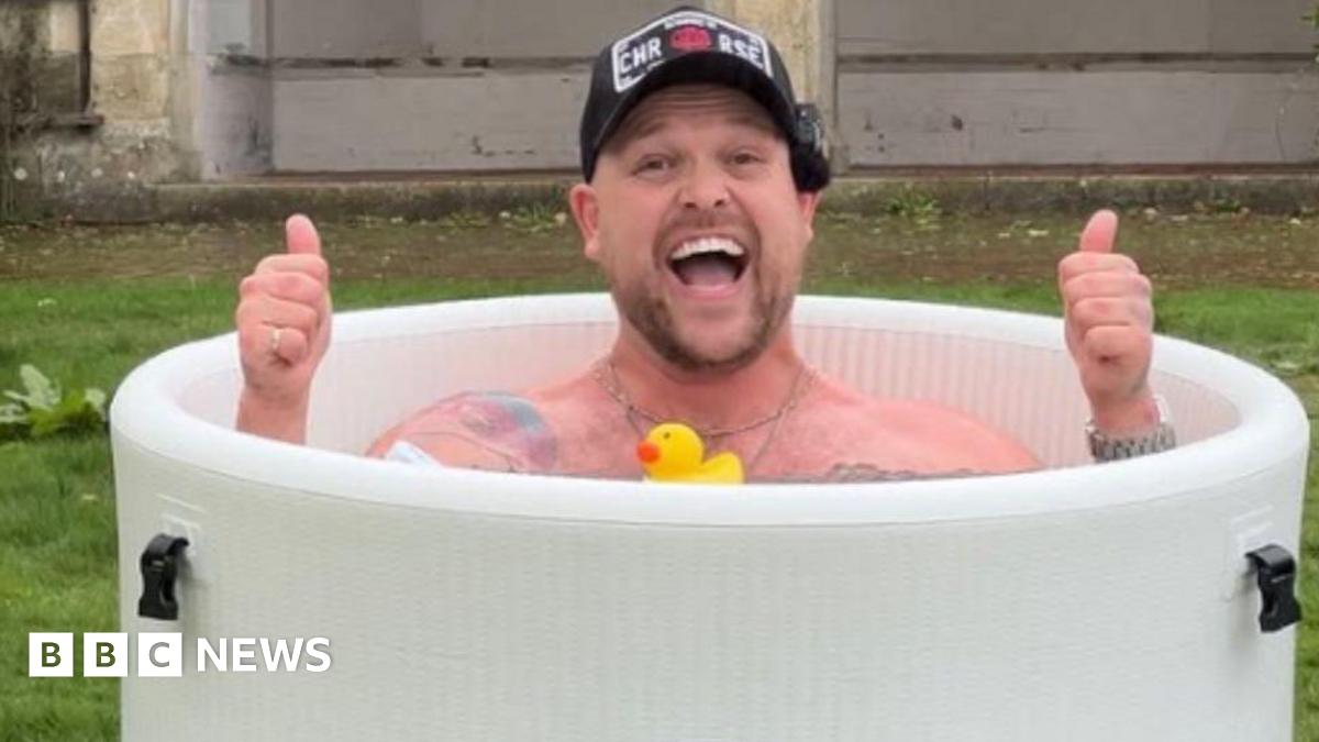 Image of Harry Beattie in a round ice bath, smiling at the camera with his thumbs up, all he is wearing is a black cap.