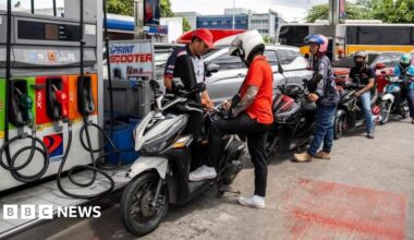 A worker helps a motorcyclist top up fuel for his bike. Behind him are more than five other bikers queuing for fuel.