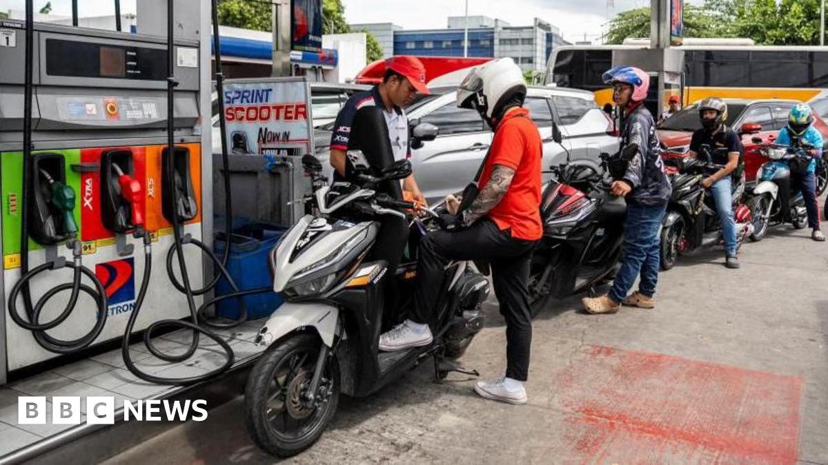 A worker helps a motorcyclist top up fuel for his bike. Behind him are more than five other bikers queuing for fuel.
