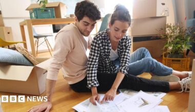 Young couple sit on the floor surrounded by boxes and paperwork.