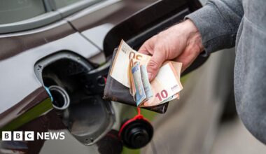 A man holding euro notes and a wallet in front of an open petrol cap of a dark coloured car.