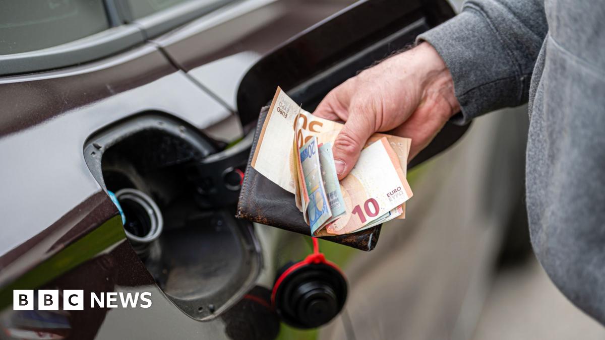 A man holding euro notes and a wallet in front of an open petrol cap of a dark coloured car.