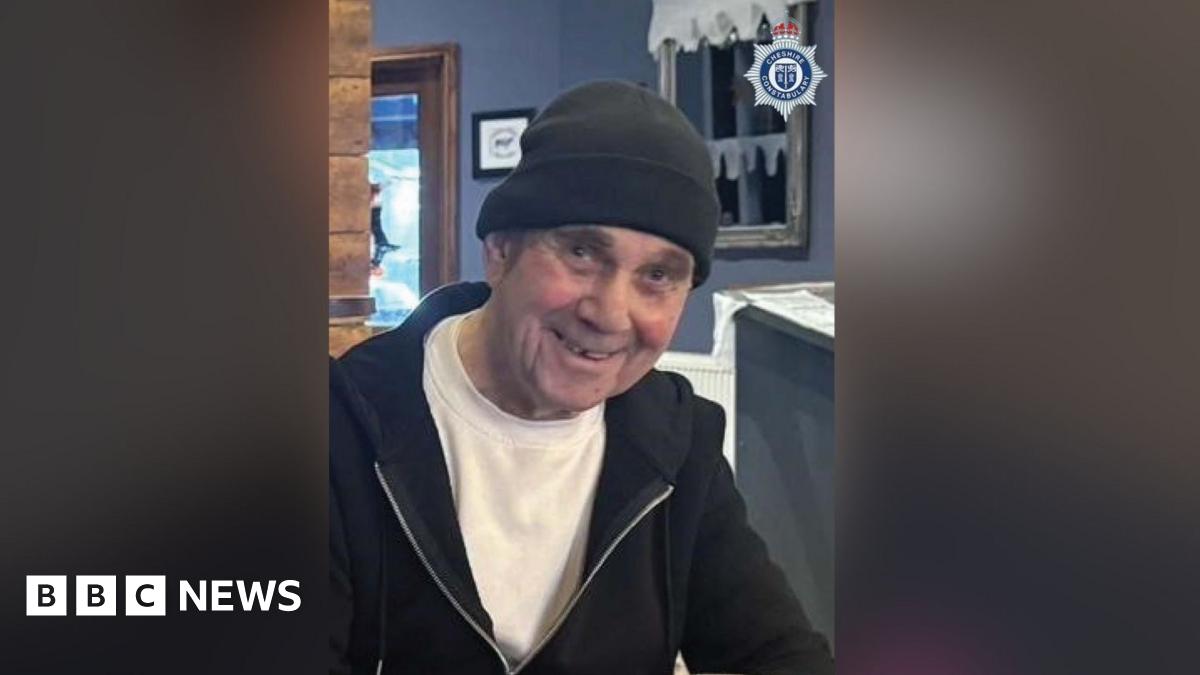 John McColl is seen smiling waring a black beanie hat, t-shirt and black hoodie.