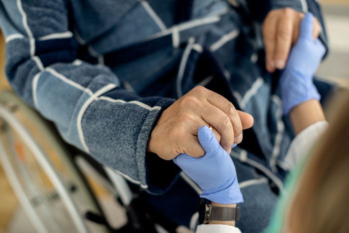 Doctor wearing blue gloves holding hand of patient in wheelchair, highlighting diseases people should fear more.