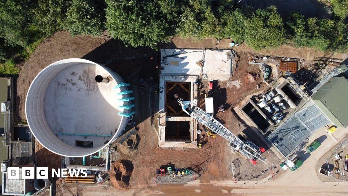 A woman with dark hair and a multiple colour jumper siting on a green sofa inside her living room.