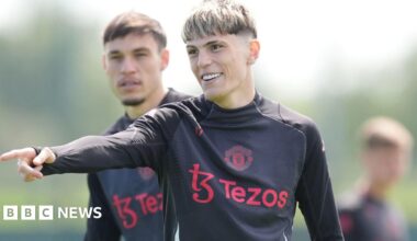 Garnacho has short dyed blonde hair and is wearing a black training top with red sponsor logo and Manchester United badge - it is a shot from training in 2025.