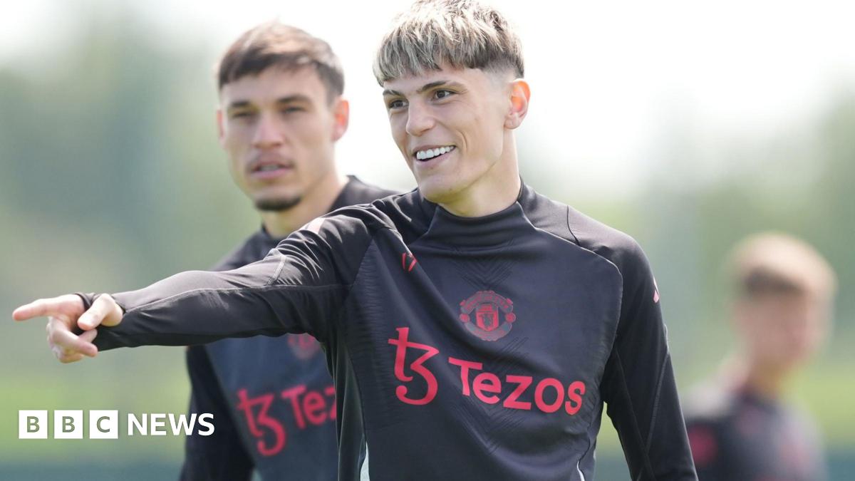 Garnacho has short dyed blonde hair and is wearing a black training top with red sponsor logo and Manchester United badge - it is a shot from training in 2025.
