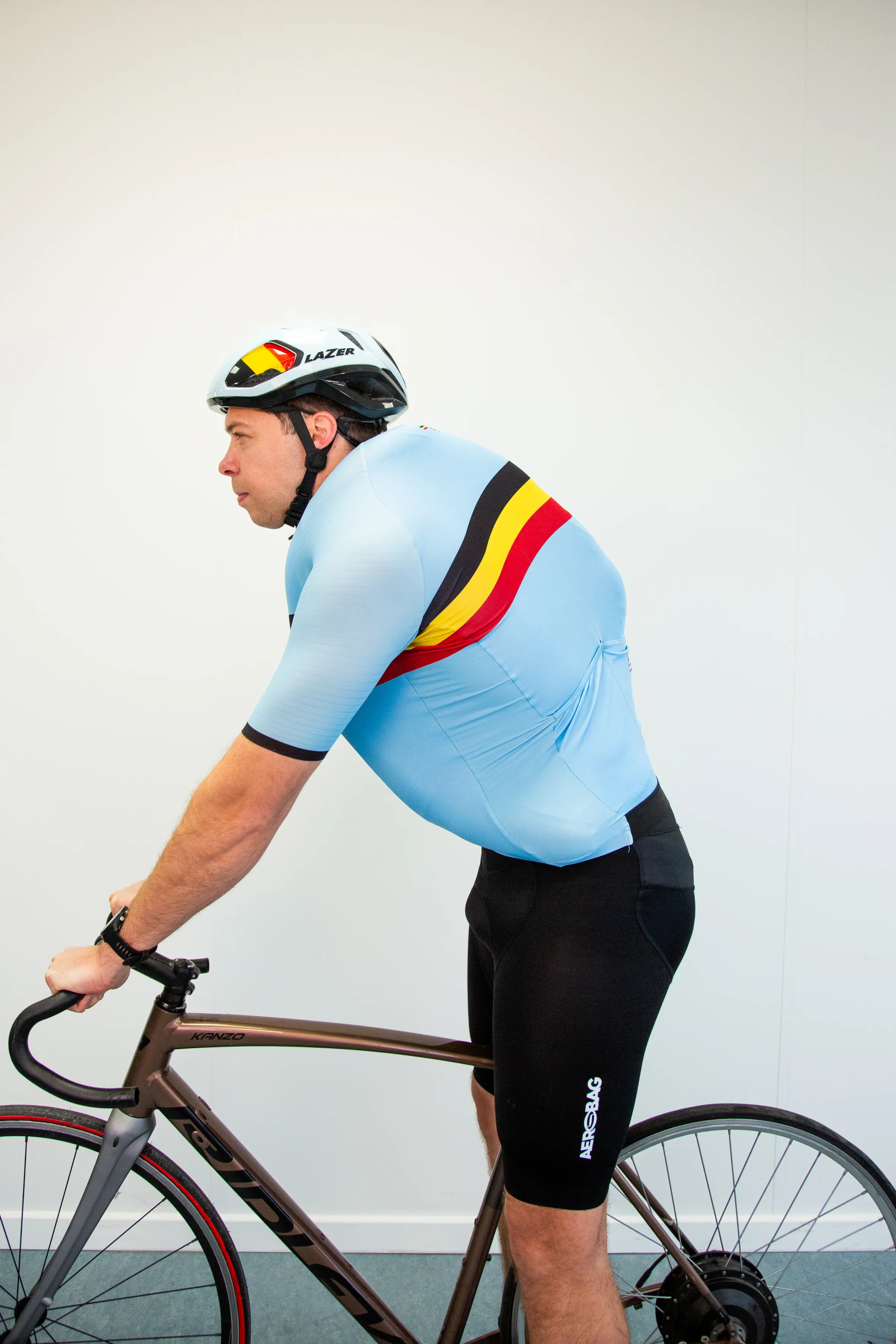 A cyclist in a light blue jersey with black, yellow, and red stripes, wearing a white and black helmet, testing an airbag cycling suit.