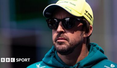 Fernando Alonso wearing sunglasses, an Aston Martin hoodie and a yellow cap