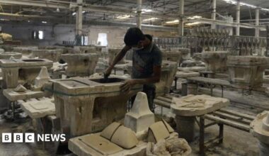 A man works on a toilet seat at a ceramic factory in Gujarat's Morbi in November 2016. He is in a large factory hall, surrounded by a large number of finished and unfinished sanitaryware.