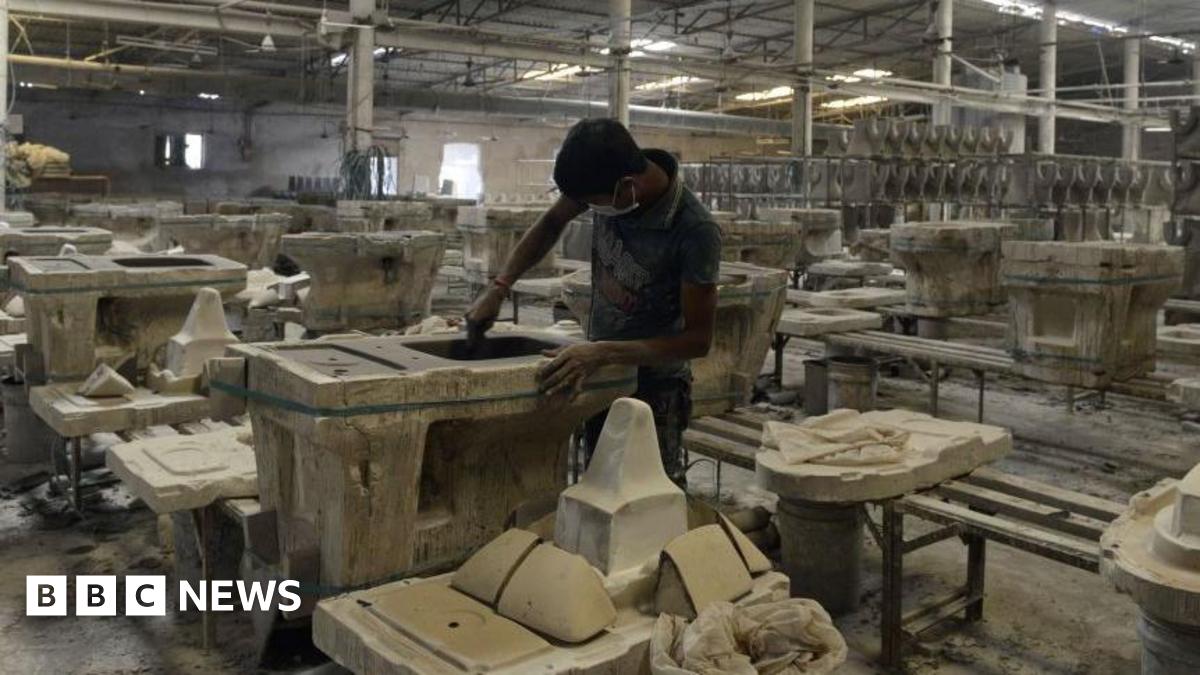 A man works on a toilet seat at a ceramic factory in Gujarat's Morbi in November 2016. He is in a large factory hall, surrounded by a large number of finished and unfinished sanitaryware.