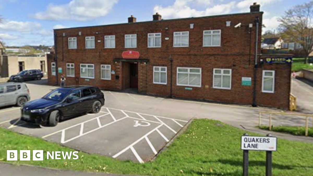 A two-storey brick built building stands surrounded by a car park and grassy area.