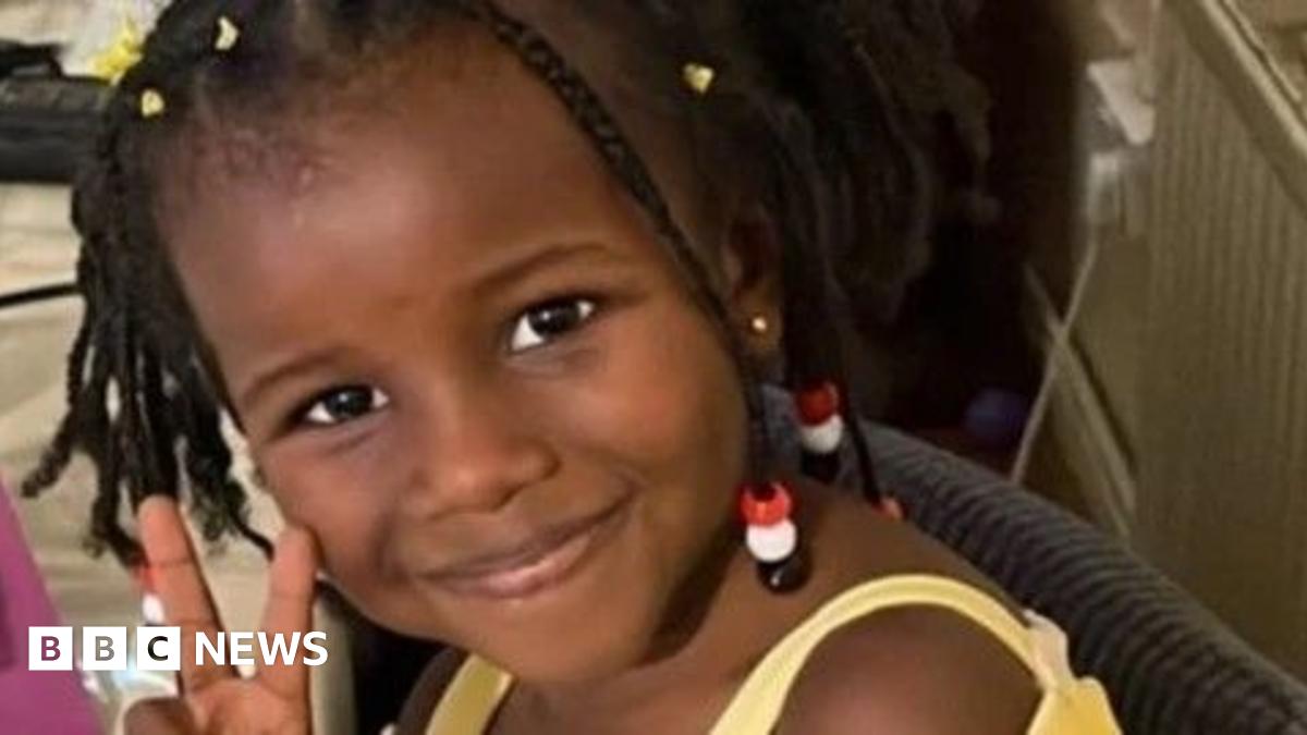 A woman with dark hair and a multiple colour jumper siting on a green sofa inside her living room.