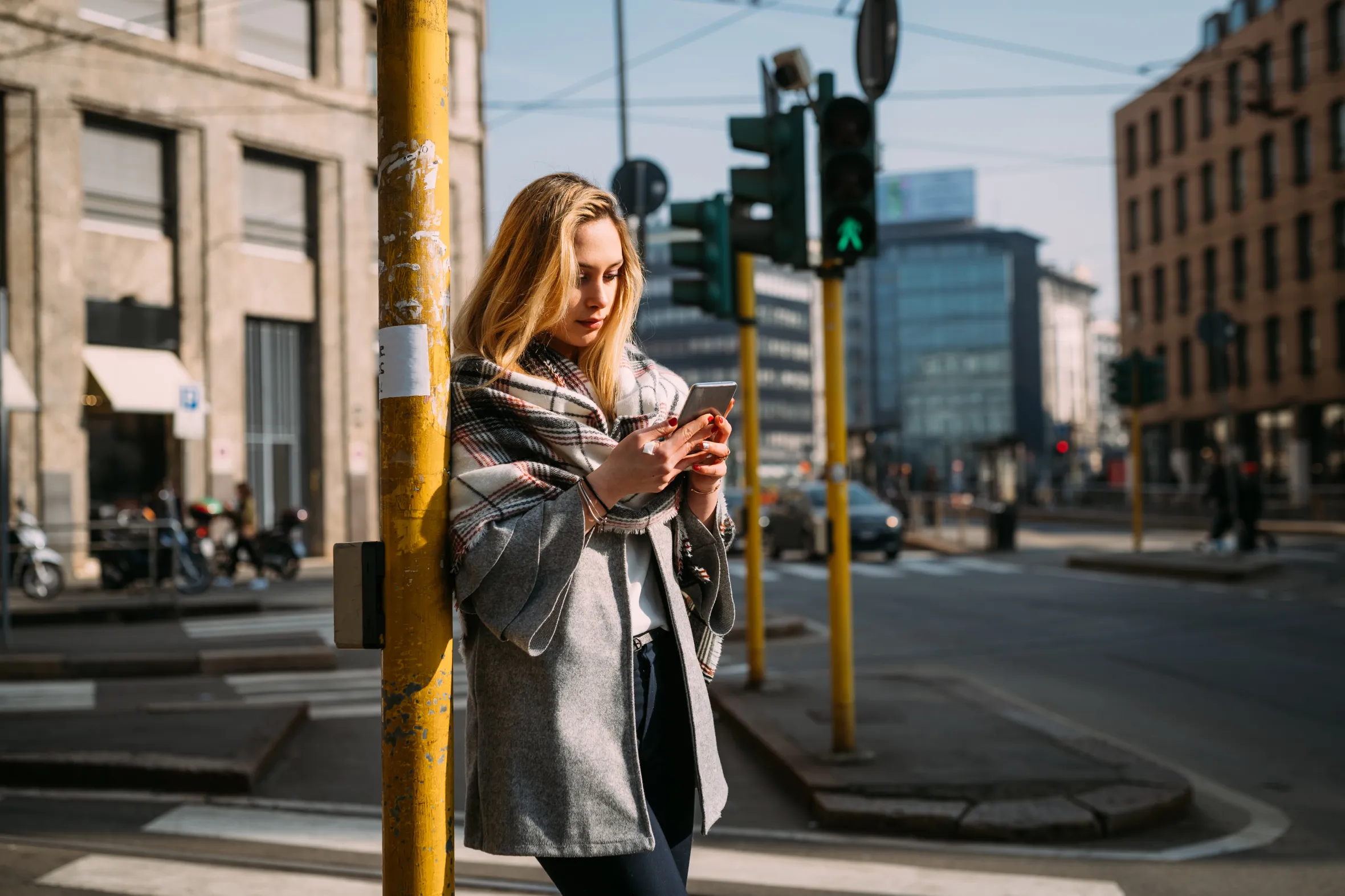 Young female tourist at a tram station in Milan, Italy, looking at her smartphone.