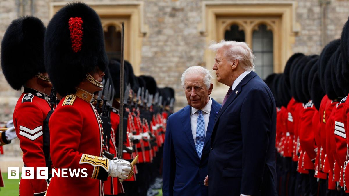 President Donald Trump and King Charles inspect a Guard of Honour together. The pair, both wearing dark suits, are stood between two rows of Beefeaters, dressed in red and with tall black headwear.
