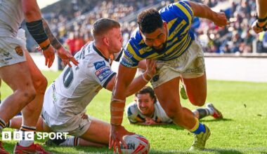 Warrington forward Kelepi Tanginoa, in primrose and blue, touches down the ball for his hat-trick try as a Castleford player in all-white tries to stop him and two more look on.