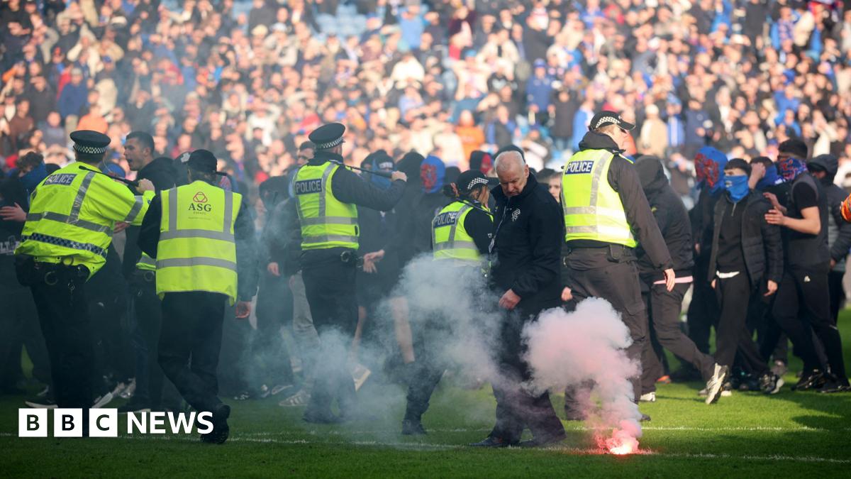 A line of police on the pitch at Ibrox during an invasion of both Celtic and Rangers fans. A flare burns on the pitch in the foreground