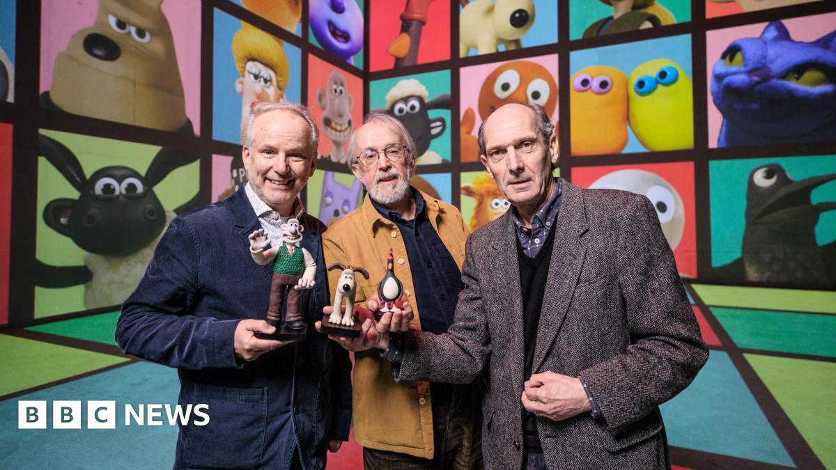 Aardman animation's co-founder and creators are standing in front of screen showing a collection of the studios most famous characters, including Wallace & Gromit, Shaun the Sheep and Morph. Peter Lord is standing in the middle wearing a brown Jacket holding a Gromit figurine. Nick Park is standing to the left of him wearing a navy blazer and holding a Wallace figurine and David Sproxton is standing to the right of Peter holding a penguin figurine.