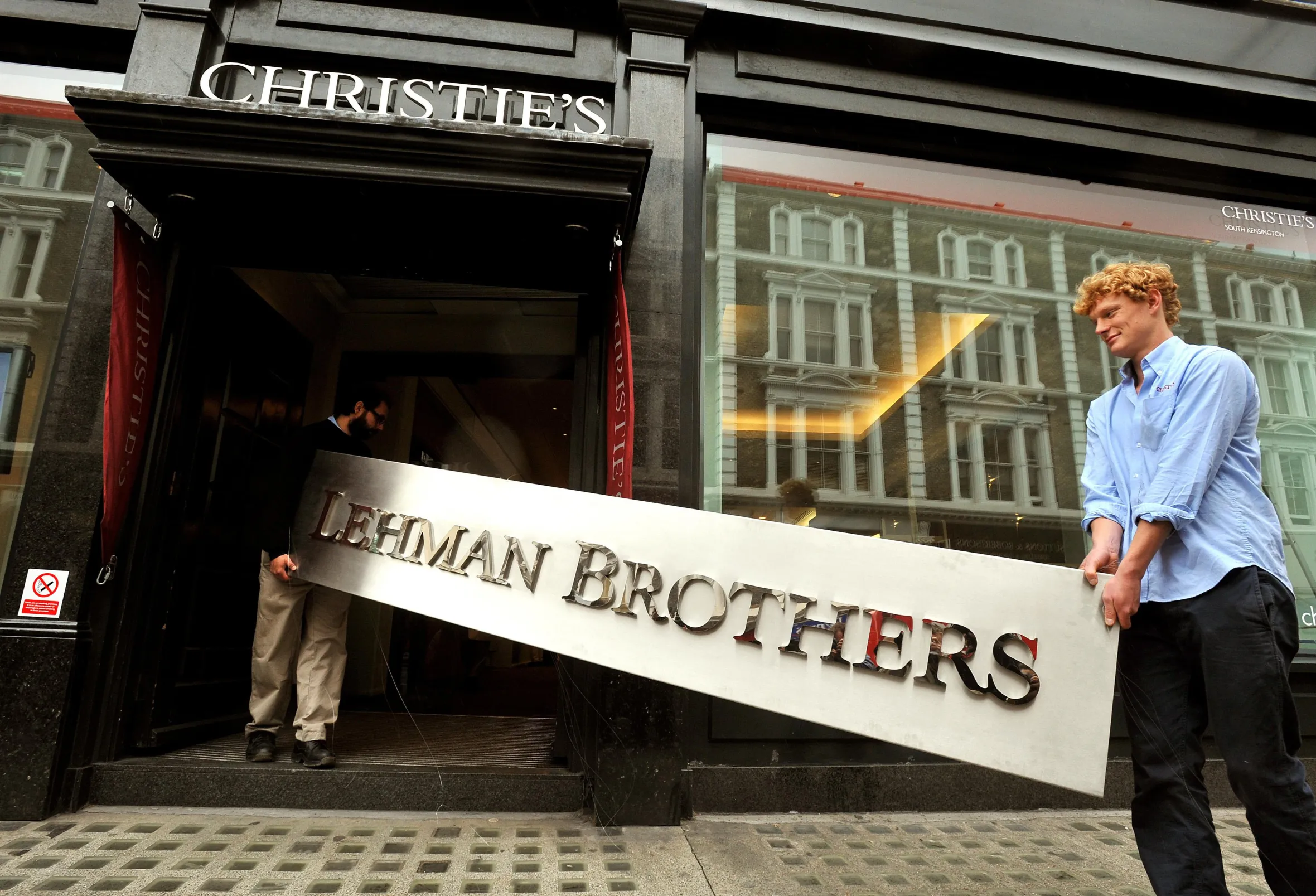 Two men carrying the "Lehman Brothers" sign into a Christie's auction house.