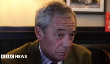 Nigel Farage - Reform UK leader - in a Leeds pub wearing a green jacket, checked white shirt, and maroon tie