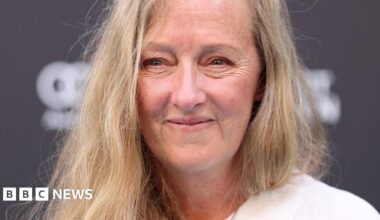 A close up of a middle-aged woman with long blonde hair, smiling at the camera.