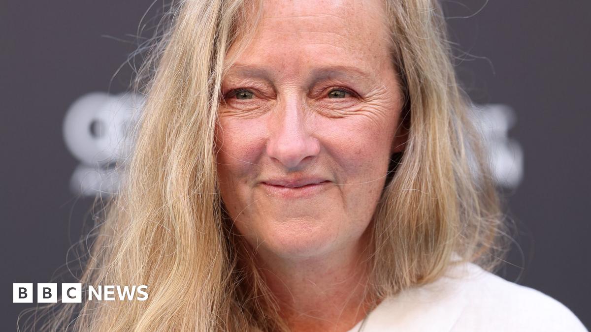A close up of a middle-aged woman with long blonde hair, smiling at the camera.