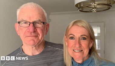 Chris and Rosie McGrane stand together in their house looking into the camera.